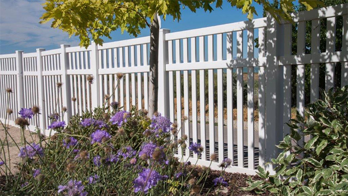 White closed picket fencing behind purple flowers, some of our best vinyl fence panels near Sanger, California.