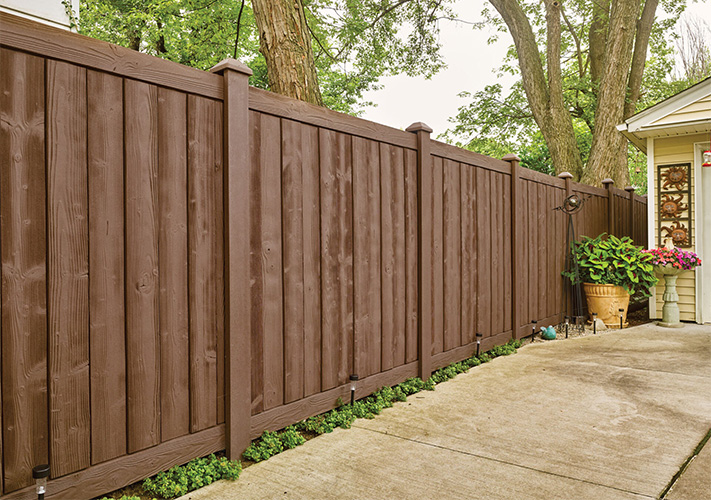 A stretch of brown Sherwood SimTek composite fence panels to the left of a home garage, an example of our Dinuba molded plastic fencing.