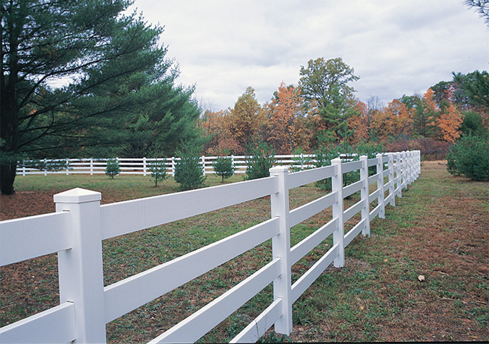 White 4-rail ranch rail fences near West Hills creating perimeter in grassy area with trees.