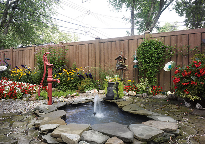 Brown faux wood fence panels near Bakersfield, California, behind a garden and mini pond.